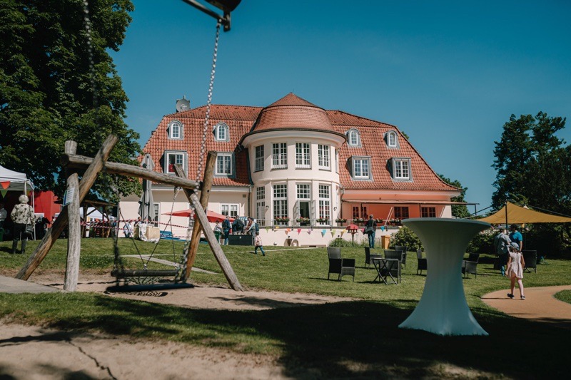 Ein Gebäude mit rotem Dach und großen Fenstern in einem Gartenbereich mit Spielplatz.