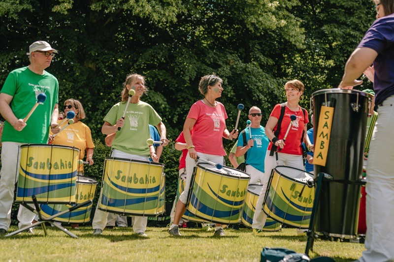 Eine Gruppe von Musiker:innen in bunten T-Shirts spielt auf großen Trommeln im Freien.