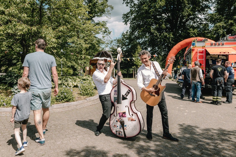 Zwei Musiker, einer mit einem Kontrabass und der andere mit einer Gitarre, posieren im Freien.