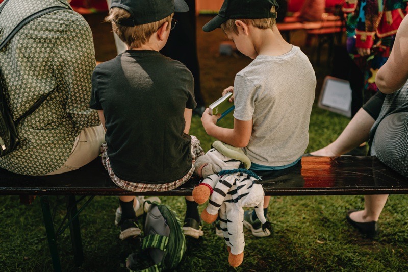 Zwei Kinder sitzen auf einer Bank, eines hält ein Buch in der Hand.
