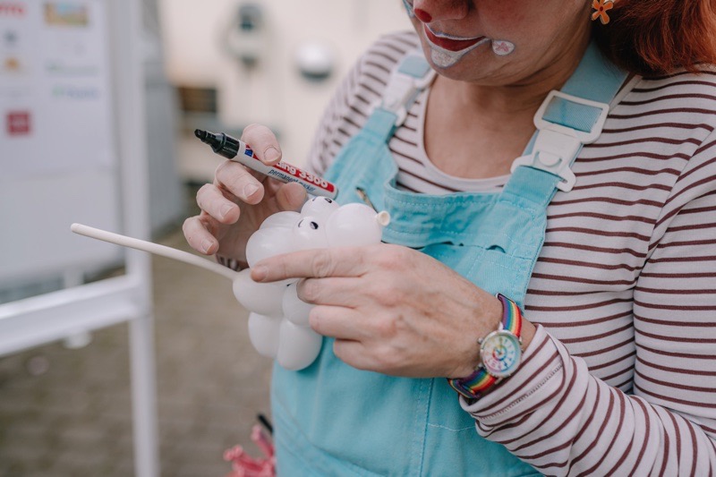 Person mit Clowns-Makeup mit gestreiftem Oberteil, die einen Ballon mit einem Marker bemalt.