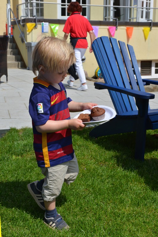 Ein Junge in einem Fußballtrikot trägt einen Teller mit Kuchen im Freien.