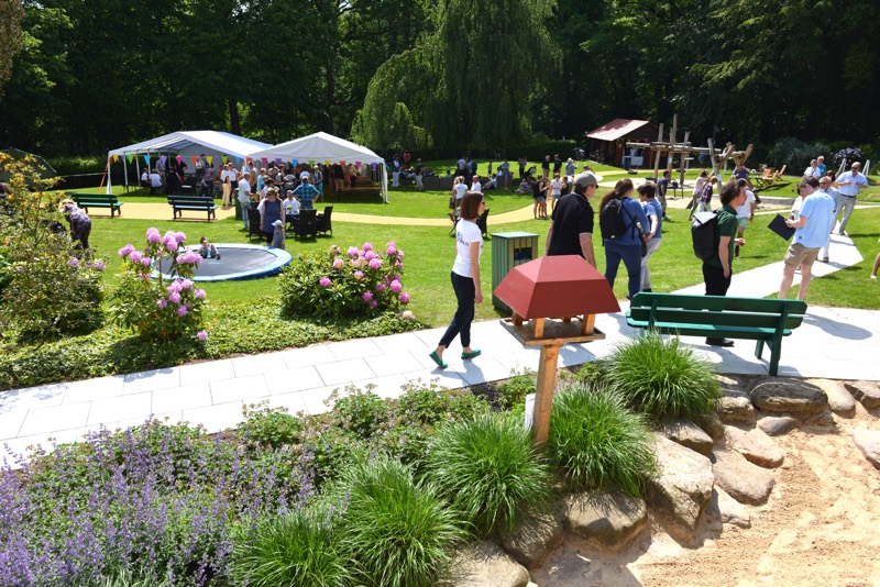 Menschen versammeln sich auf einer Wiese während eines Sommerfestes mit Zelten und Spielgeräten.