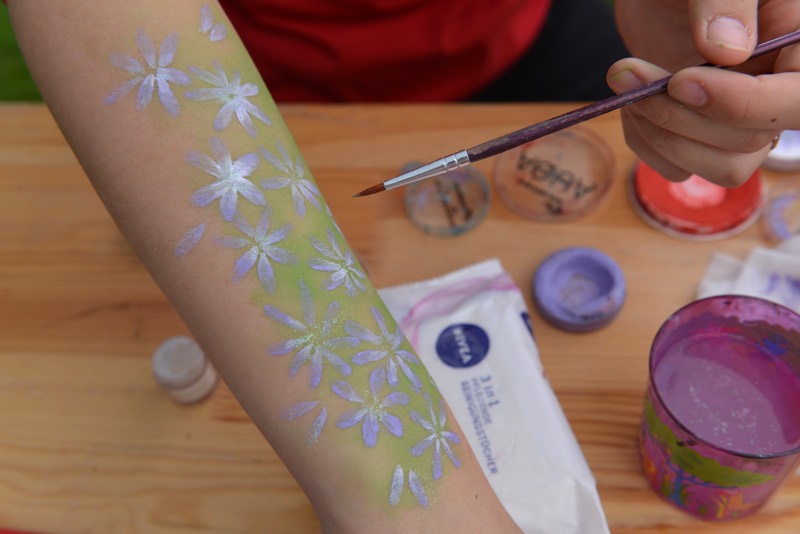 Ein bemalter Arm mit lila und grünen Blumenmustern.