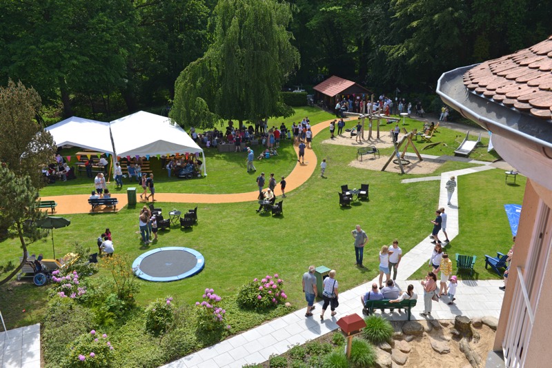 Ansicht eines Sommerfestes mit Zelten, Spielgeräten und Menschen im Freien.