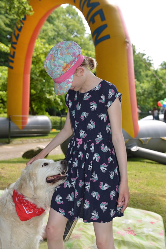Ein Mädchen in einem Kleid mit Einhorn-Muster steht neben einem Golden Retriever, der ein rotes Halstuch trägt.