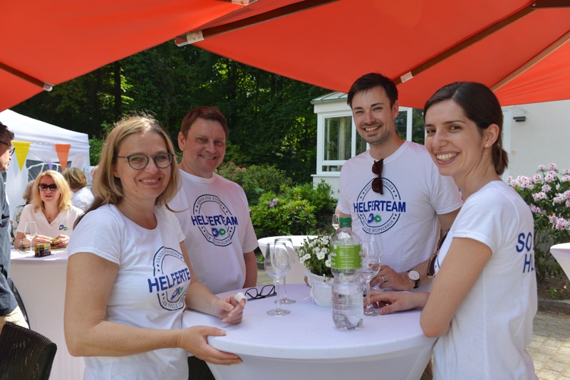 Vier Personen in weißen T-Shirts mit der Aufschrift 'Helferteam' stehen an einem Stehtisch.