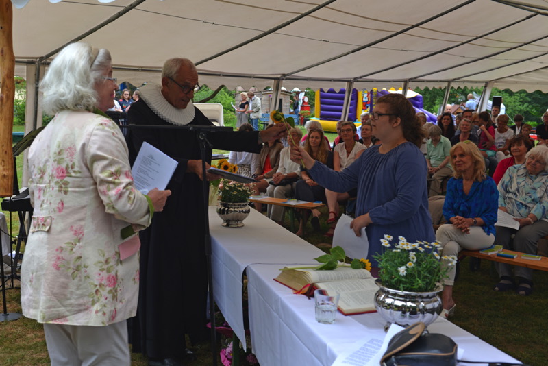 Personen in einem Zelt bei einer Veranstaltung. Ein Pastor überreicht einer Frau eine Sonnenblume.