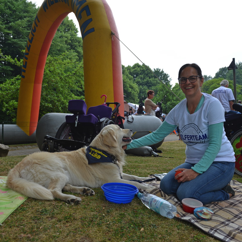 Frau mit Brille sitzt auf einer Decke neben einem Golden Retriever, der auf dem Boden liegt.
