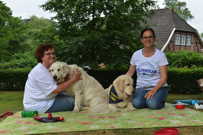 Zwei Frauen mit zwei Golden Retrievern auf einer Decke im Freien.