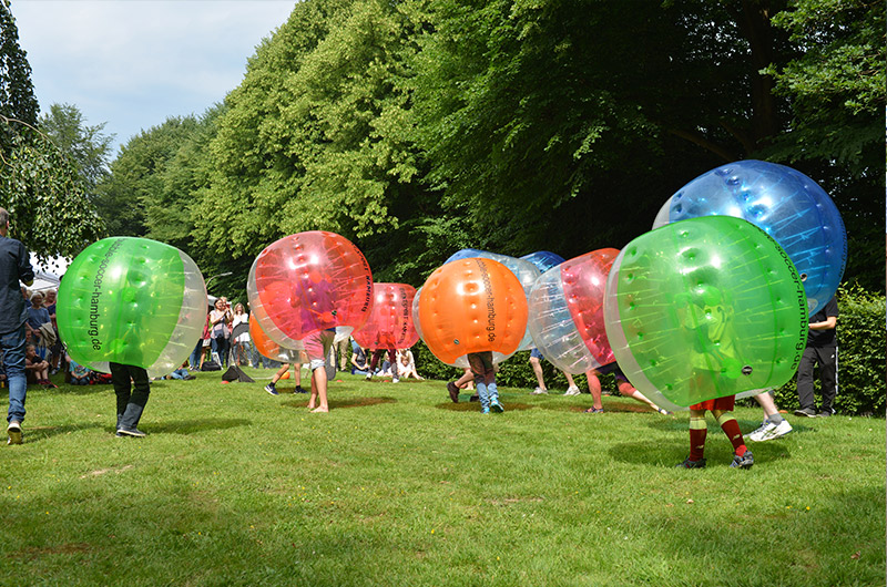 Kinder in aufblasbaren, bunten Bällen, die im Freien spielen und sich bewegen.