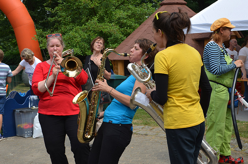 Drei Musikerinnen spielen verschiedene Blasinstrumente bei einer Veranstaltung im Freien.