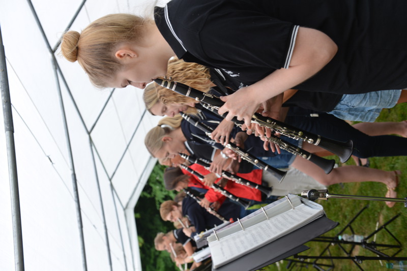 Gruppe von Musiker:innen, die Klarinetten unter einem Zelt spielen, während sie auf Notenblätter schauen.