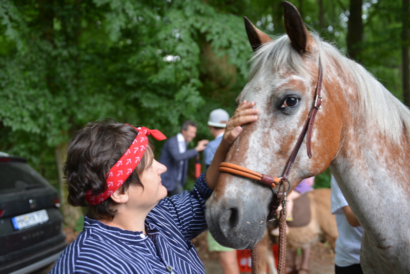 Eine Frau mit einem roten Bandana streichelt ein grau-braun geschecktes Pferd.