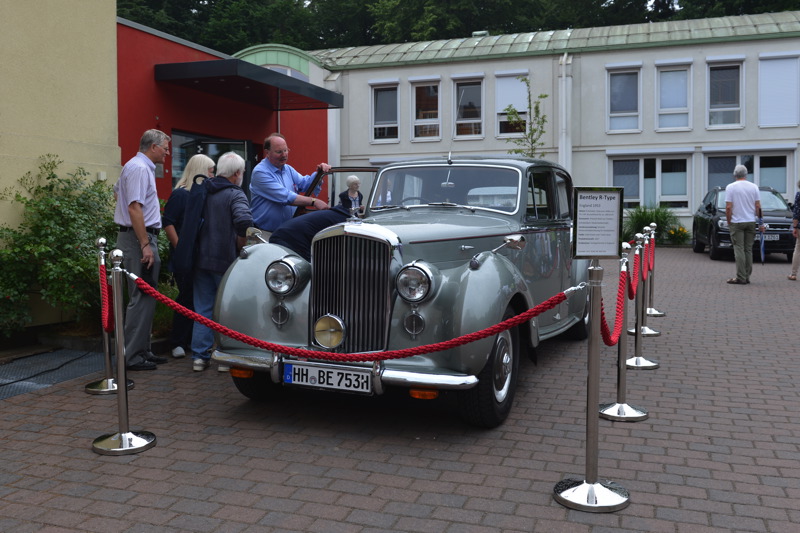 Silberner Bentley mit roten Absperrungen und Menschen, die das Auto betrachten.