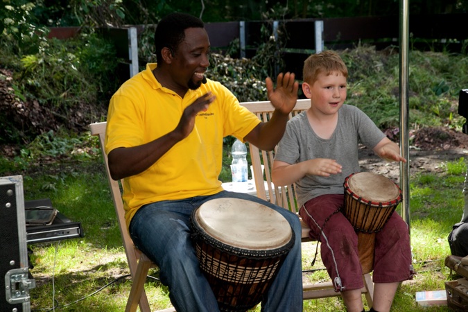Ein Mann und ein Junge sitzen auf Stühlen und spielen Trommeln im Freien.
