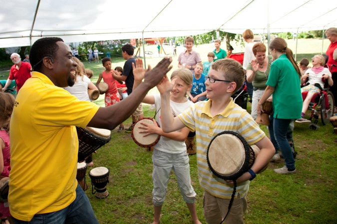 Ein Mann und Kinder trommeln zusammen unter einem Zelt.