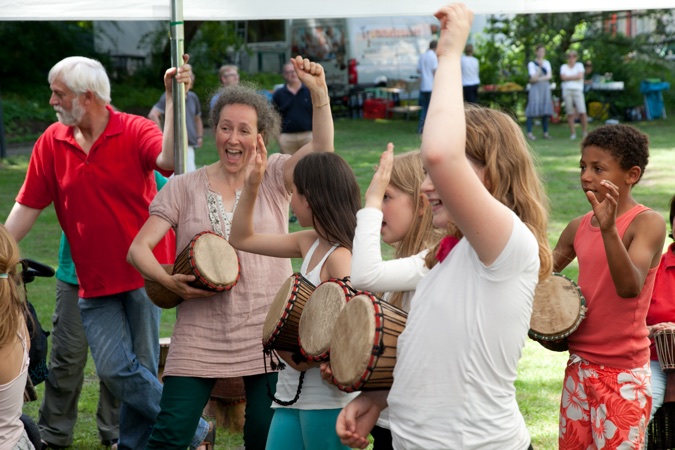 Menschen, die bei einer Veranstaltung zusammen trommeln und tanzen, mit verschiedenen Trommeln in der Hand.