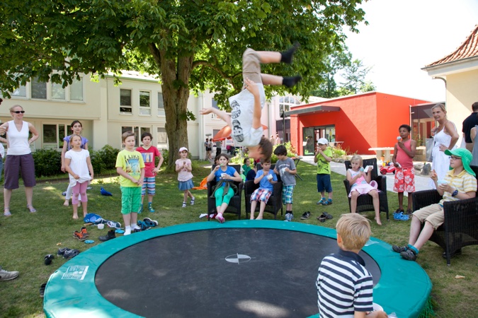 Ein Kind springt auf einem Trampolin, während andere Kinder und Erwachsene zuschauen.