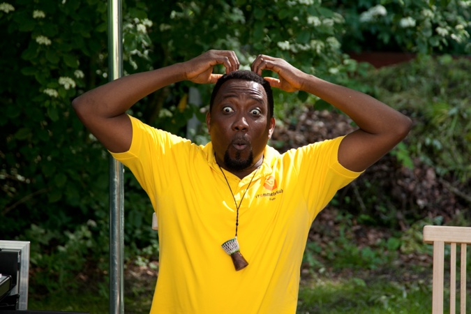 Mann mit überrascht wirkendem Gesichtsausdruck und Händen auf dem Kopf in einem gelben T-Shirt.