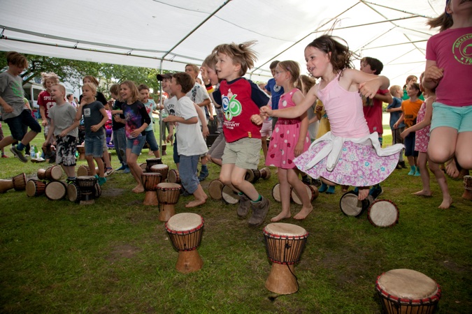 Gruppe von Kindern, die zwischen Trommeln in einem Zelt hüpfen und spielen.