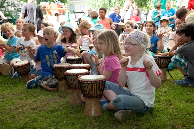 Gruppe von Kindern, die auf Trommeln spielen, während sie lächeln und klatschen.