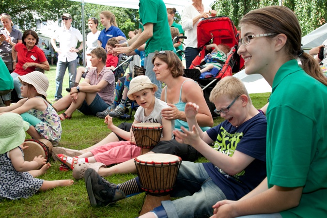 Kinder und Erwachsene sitzen im Freien und spielen Trommeln während einer Veranstaltung.