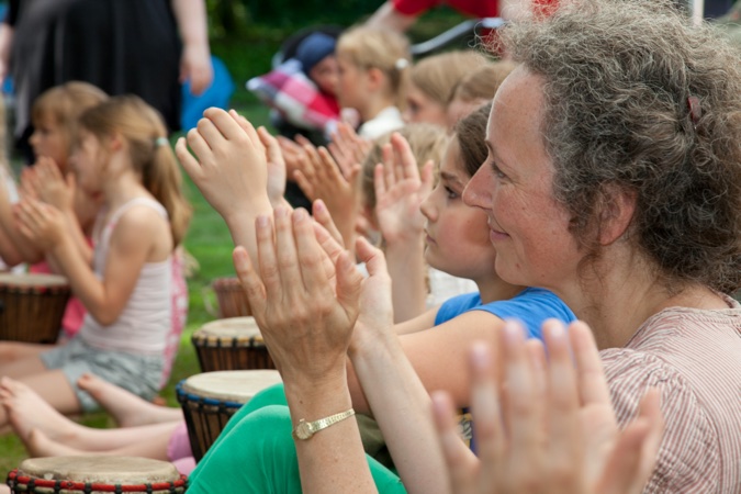 Gruppe von Frauen und Kindern, die beim Trommeln in einer Reihe sitzen und klatschen.