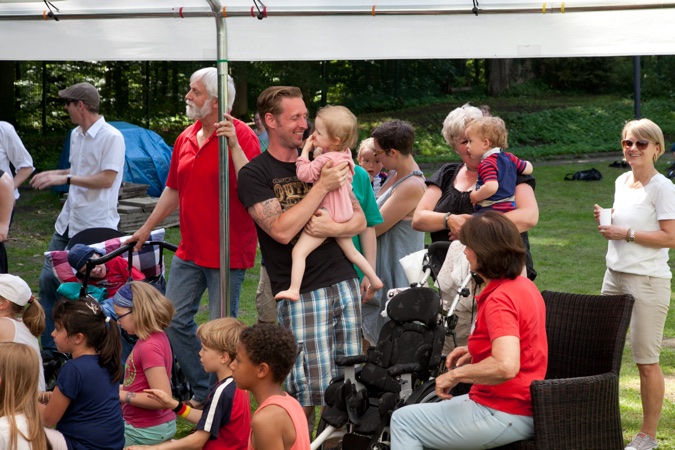 Gruppe von Menschen, darunter Erwachsene und Kinder, bei einer Veranstaltung im Freien unter einem Zelt.