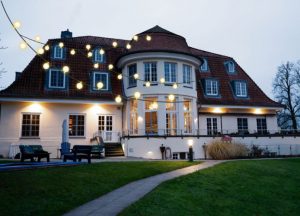 Ein großes, hell erleuchtetes Gebäude mit runden Fenstern und einer auffälligen Dachform, umgeben von Lichtern.