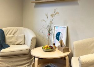 Ein kleiner Tisch mit einer Schale Obst und einer Vase in einem Sitzbereich mit zwei Stühlen.