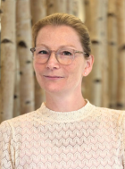 Porträt einer Frau mit blonden Haaren und Brille, die in die Kamera schaut.