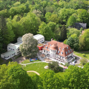Luftaufnahme eines großen, mehrstöckigen Gebäudes mit rotem Dach und umgebender grüner Landschaft.