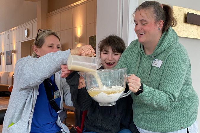 Drei Frauen, die gemeinsam Teig in einer großen Schüssel vorbereiten.