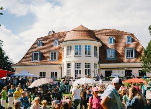 Veranstaltungsort mit einer großen Menschenmenge vor einem historischen Gebäude mit einem runden Turm und einem roten Dach.