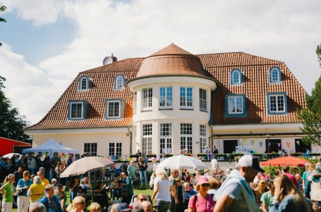 Veranstaltungsort mit einer großen Menschenmenge vor einem historischen Gebäude mit einem runden Turm und einem roten Dach.