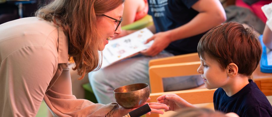 Eine Pädagog:in spricht freundlich mit einem Kind, neben einer Kupfer-Klangschale im Betreuungsumfeld von Hände für Kinder, Der Neue Kupferhof in Hamburg.