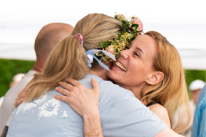 Zwei Frauen umarmen sich, eine von ihnen trägt einen Blumenkranz im Haar.