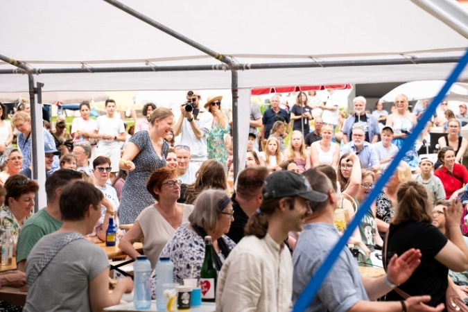 Szenisches Bild vom Publikum. Viele lächelnde Gesichter und mittendrin ein Mann mit einer Kamera.