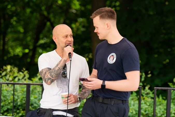 Jürgen Vögel steht mit Mikrofon in der Hand auf einer Bühne und schaut einem jungen Mann von der Freiwilligen Feuerwehr ins Gesicht, während er gerade spricht.