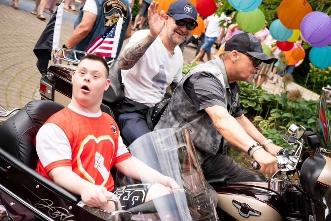 Ein Junge sitzt im Beiwagen einer Harley-Davidson und ist erstaunt. Neben ihm sitzt der Motorrad-Fahrer und hält das Lenkrad fest, dahinter sitzt Jürgen Vogel und winkt.