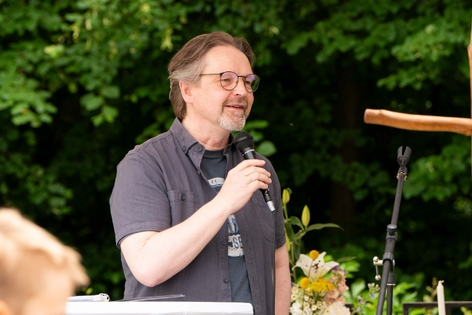 Pastor Bastian Meyer mit Mikrofon in der Hand. Er steht auf der Bühne und schaut zum Publikum.