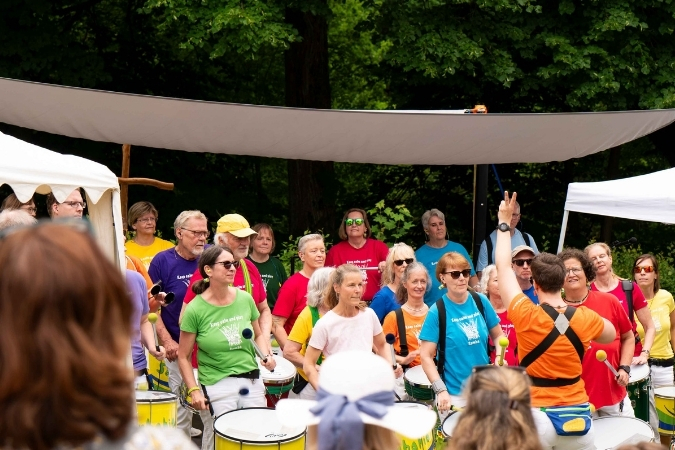 Eine Gruppe aus Trommlerinnen und Trommlern in Aktion. Sie sind bunt gekleidet und haben die Trommeln um ihren Bauch und halten die Schläger in den Händen.