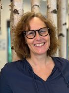 Sandra Baruschke lächelt in einem Porträt mit Brille und blauem Oberteil.