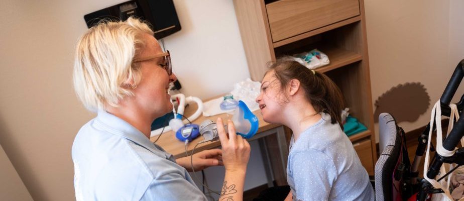 Eine weibliche Pflegekraft hält einem Mädchen eine blaue Atemmaske über Mund und Nase.